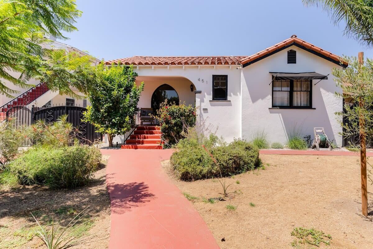 A two-story house with a red-tiled roof, a white exterior, and a red pathway leading to the entrance.