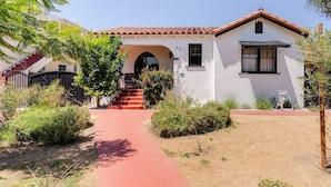 A two-story house with a red-tiled roof, a white exterior, and a red pathway leading to the entrance.