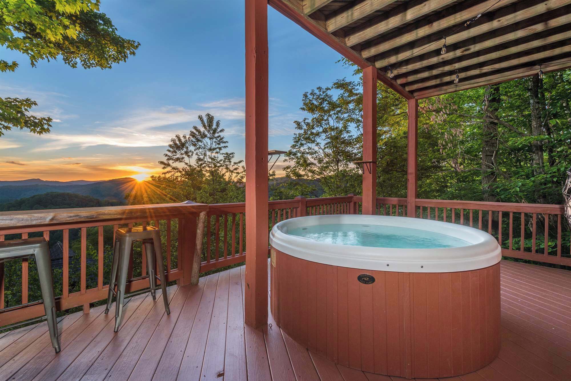 Ein Whirlpool auf einer Holzterrasse mit Blick auf Berge und Bäume.