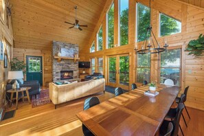 A log cabin interior with a stone fireplace, a dining area, and large windows. - The Skybox - Voted #1 Cabin in Asheville (Mars Hill)