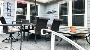 En uteplats med flätade stolar och ett bord, ett rött parasoll och en dekorativ väggdekoration.