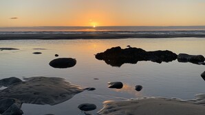 A beach scene with rocks and calm water reflecting the sunset. - Suil Na Mara - Modern Home with Mountain and Ocean Views (Tillamook County)
