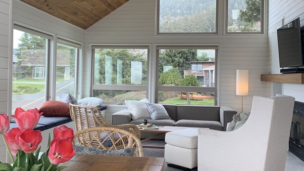 A cozy living room with a high ceiling, large windows, a fireplace, and a comfortable seating area. - Suil Na Mara - Modern Home with Mountain and Ocean Views (Tillamook County)