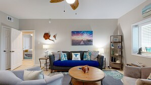 Un salon avec un canapé bleu, une table basse ronde et un ventilateur de plafond orné de motifs de feuilles.