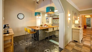 Une cuisine moderne avec un îlot central, des chaises jaunes, une horloge et des luminaires suspendus.