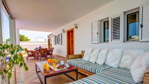Une vaste terrasse dotée d’un coin repas, d’un canapé et d’une table où sont disposés des fruits et des boissons.