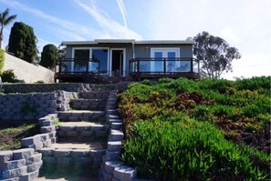 Two-story house with a balcony and stone steps leading to a landscaped garden.