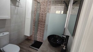 Uma casa de banho com sanita, chuveiro com porta de vidro e lavatório com cuba preta.