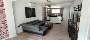 A modern living room with a grey sectional sofa, a glass coffee table, and a kitchen in the background. - El Parque Suite (Benalmádena)