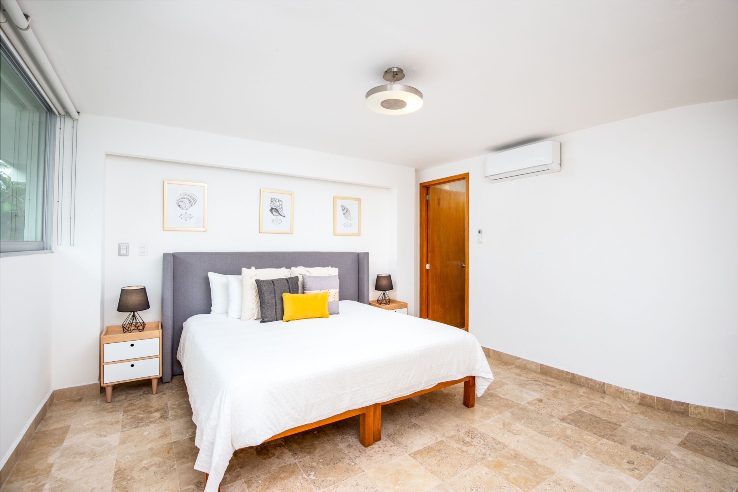 A bedroom with a bed, nightstands, a wooden door, and framed pictures on the wall.