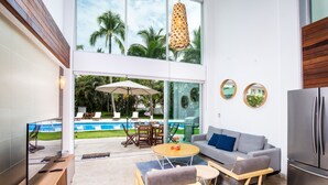 Un salón moderno con vista a la piscina, un sofá gris, una mesa de centro de madera y un televisor sobre un mueble de madera.