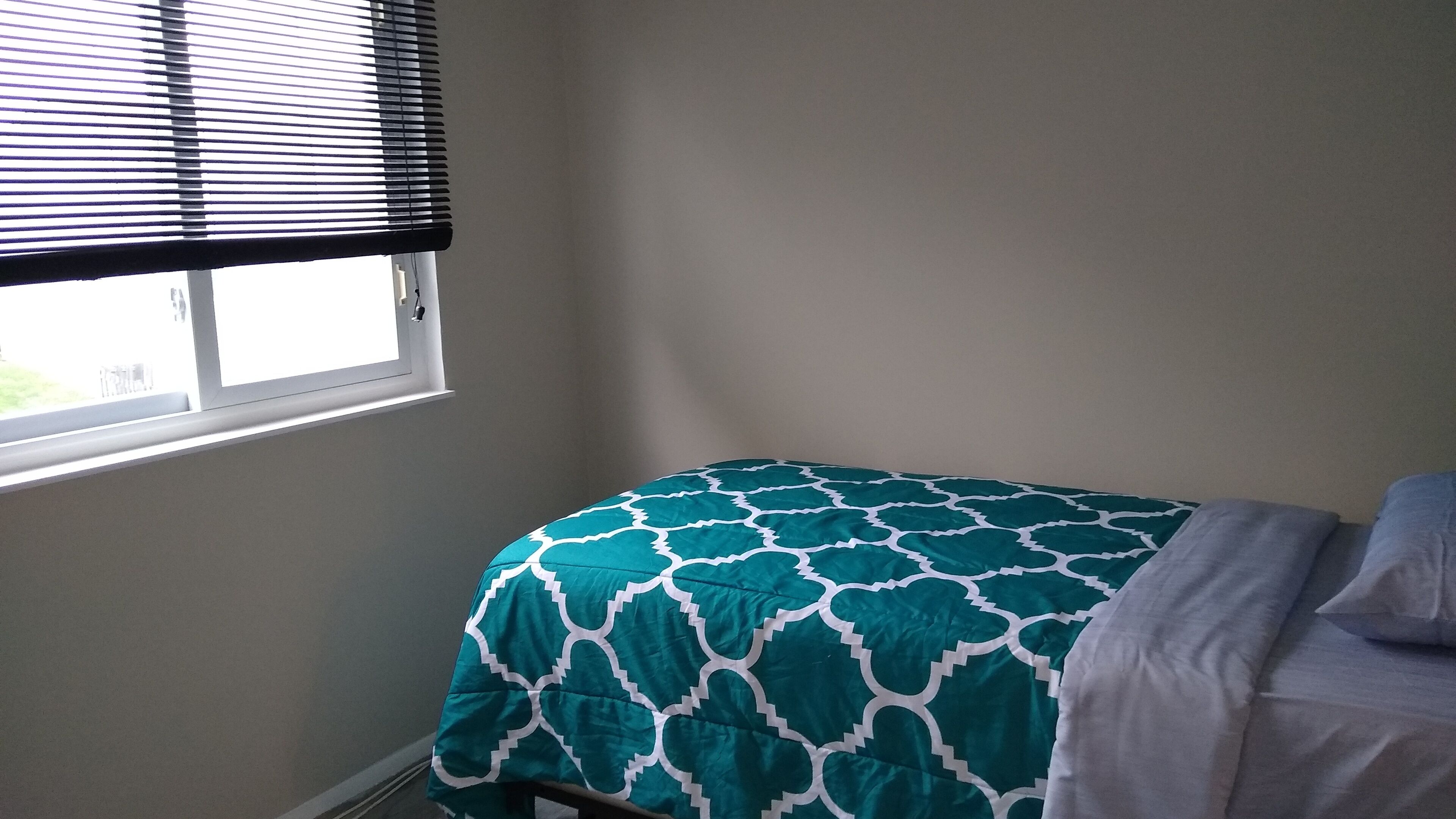 Ein Schlafzimmer mit einem Einzelbett, einem Fenster mit Jalousien und einer schlichten Wand.