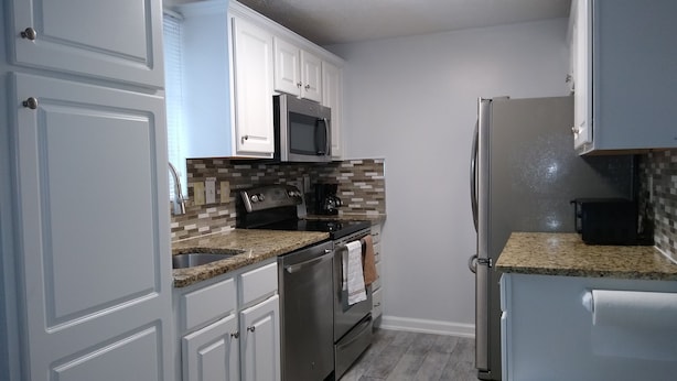 A kitchen with white cabinets, a stainless steel refrigerator, a microwave, and a stove.
