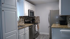A kitchen with white cabinets, a stainless steel refrigerator, a microwave, and a stove.
