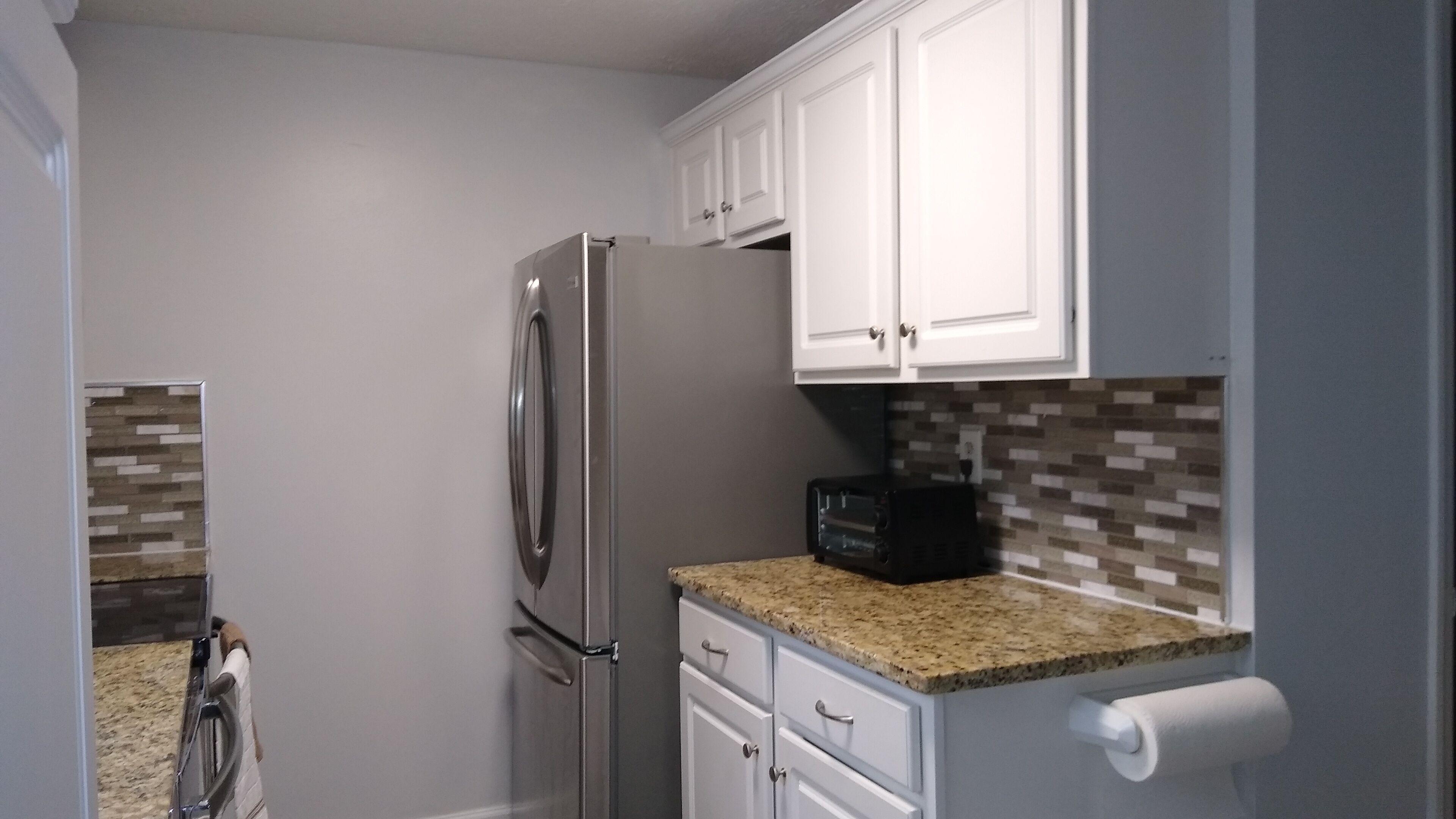 A compact kitchen with white cabinets, a stainless steel refrigerator, a microwave, and a granite countertop.