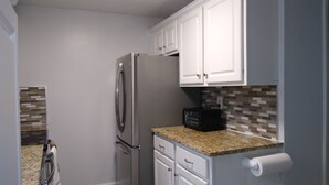 A compact kitchen with white cabinets, a stainless steel refrigerator, a microwave, and a granite countertop.