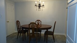 A dining room with a round table and four wooden chairs. A chandelier hangs from the ceiling.