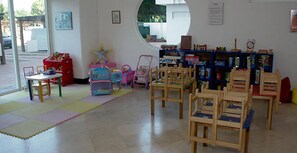 Ein Zimmer mit Holzsesseln, einem kleinen Tisch und einem Spielbereich mit Spielzeug und einem Schaukelstuhl.