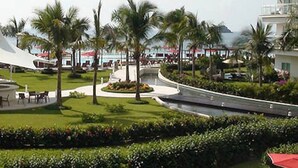A landscaped area with palm trees, a curved pathway, and a building with a white facade. - The Great Escape - Ixtapa - Penthouse on the Beach (Ixtapa Zihuatanejo)