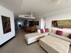 Ein modernes Wohnzimmer mit einer Eckcouch, einem Essbereich mit Stühlen und einer Küche im Hintergrund.