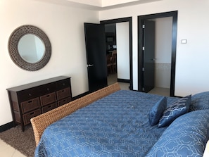 A bedroom with a bed, a dresser, a mirror, and two open doors leading to another room.