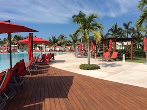 A poolside area with lounge chairs and umbrellas, palm trees, and a wooden deck.