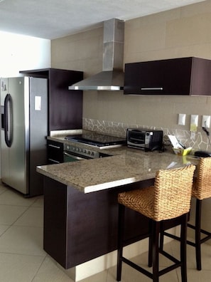 A modern kitchen with a stainless steel refrigerator, a built-in oven, a microwave, and a large island with bar stools.