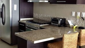A modern kitchen with dark cabinetry, a stainless steel refrigerator, a built-in oven, a microwave, and a granite countertop. - The Great Escape - Ixtapa - Penthouse on the Beach (Ixtapa Zihuatanejo)