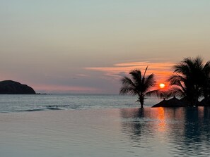 Ein Sonnenuntergang über einem ruhigen Meer mit Palmen und einer entfernten Landform.