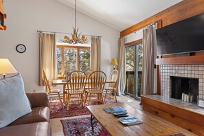A living room with a fireplace, wooden furniture, a dining area, and large windows. - Outpost: Huckleberry 3121 - Located in the Aspens! (Wilson)