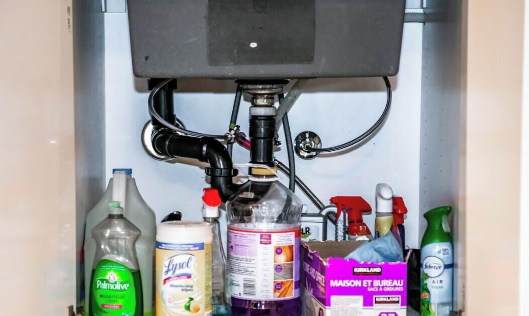 A kitchen sink with various cleaning supplies and a box of Kirkland brand dish soap.