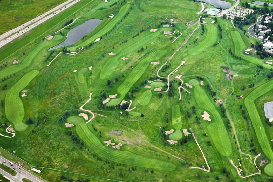 An aerial view of a golf course with multiple greens, bunkers, and a large water hazard.