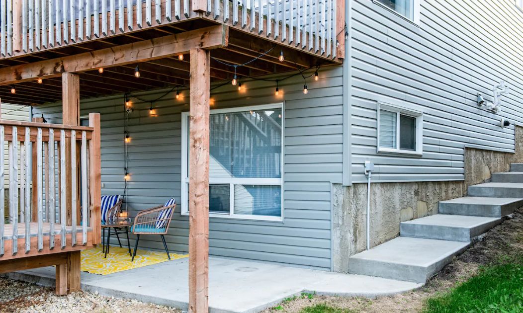 A house with a wooden deck, a concrete staircase, and a porch with chairs.