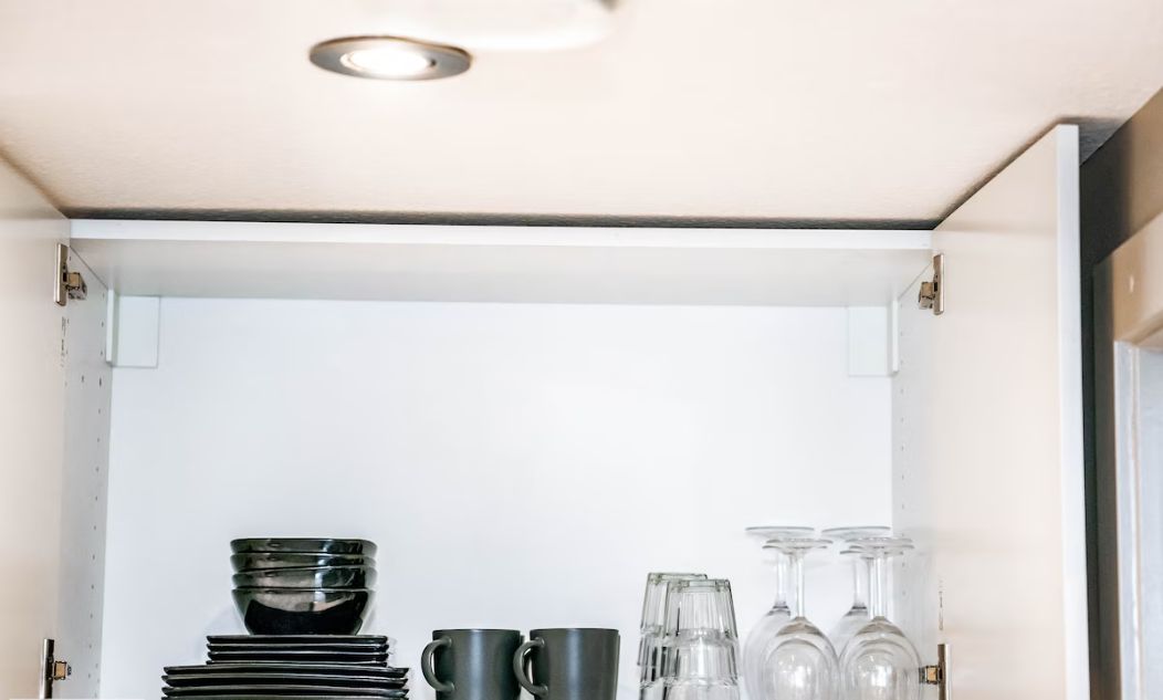 Un mueble de cocina con interior blanco, que contiene platos apilados, una taza de café y copas de vino.