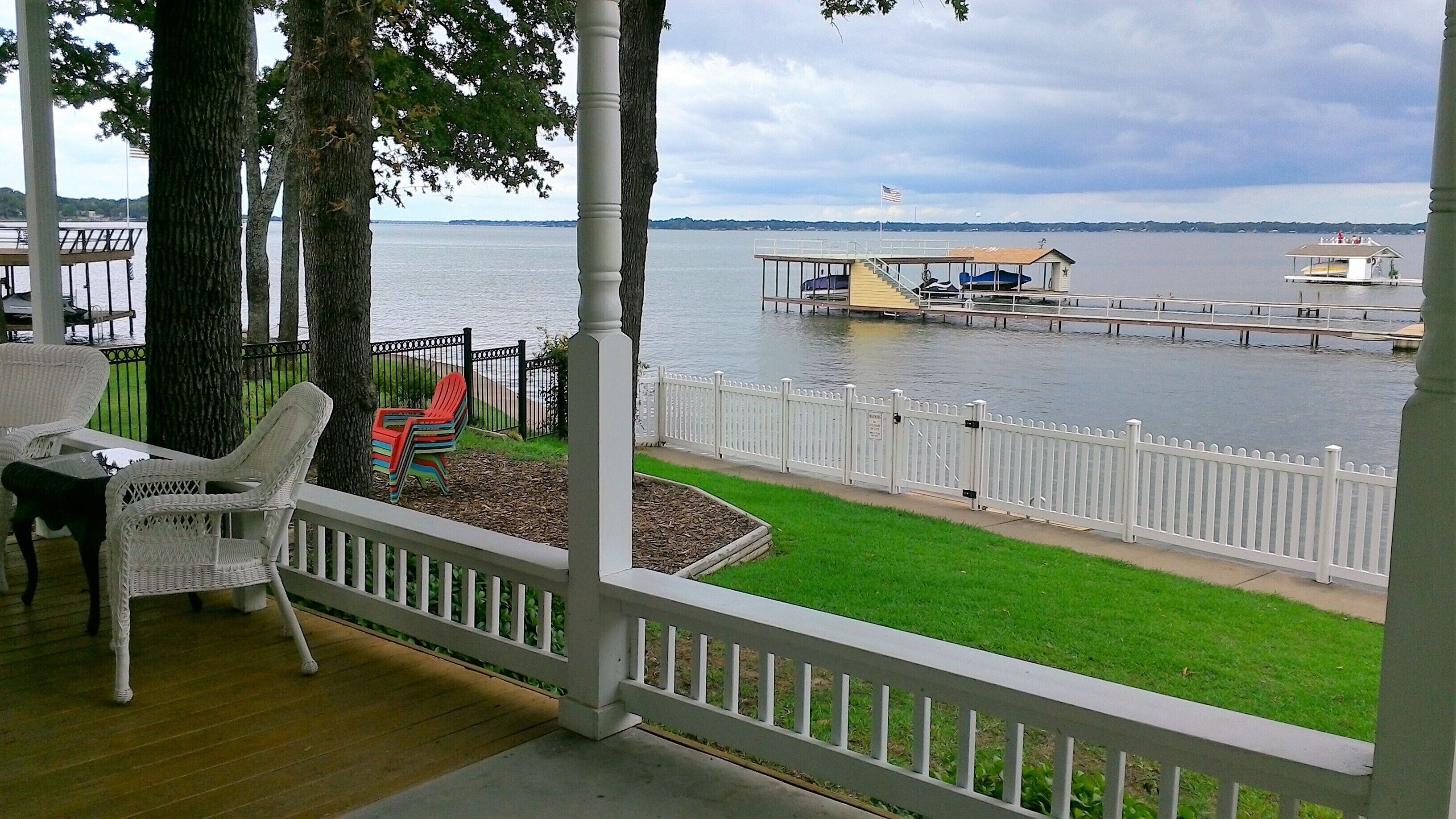 A covered outdoor area with a view of a lake, a dock with boats, and a white picket fence.