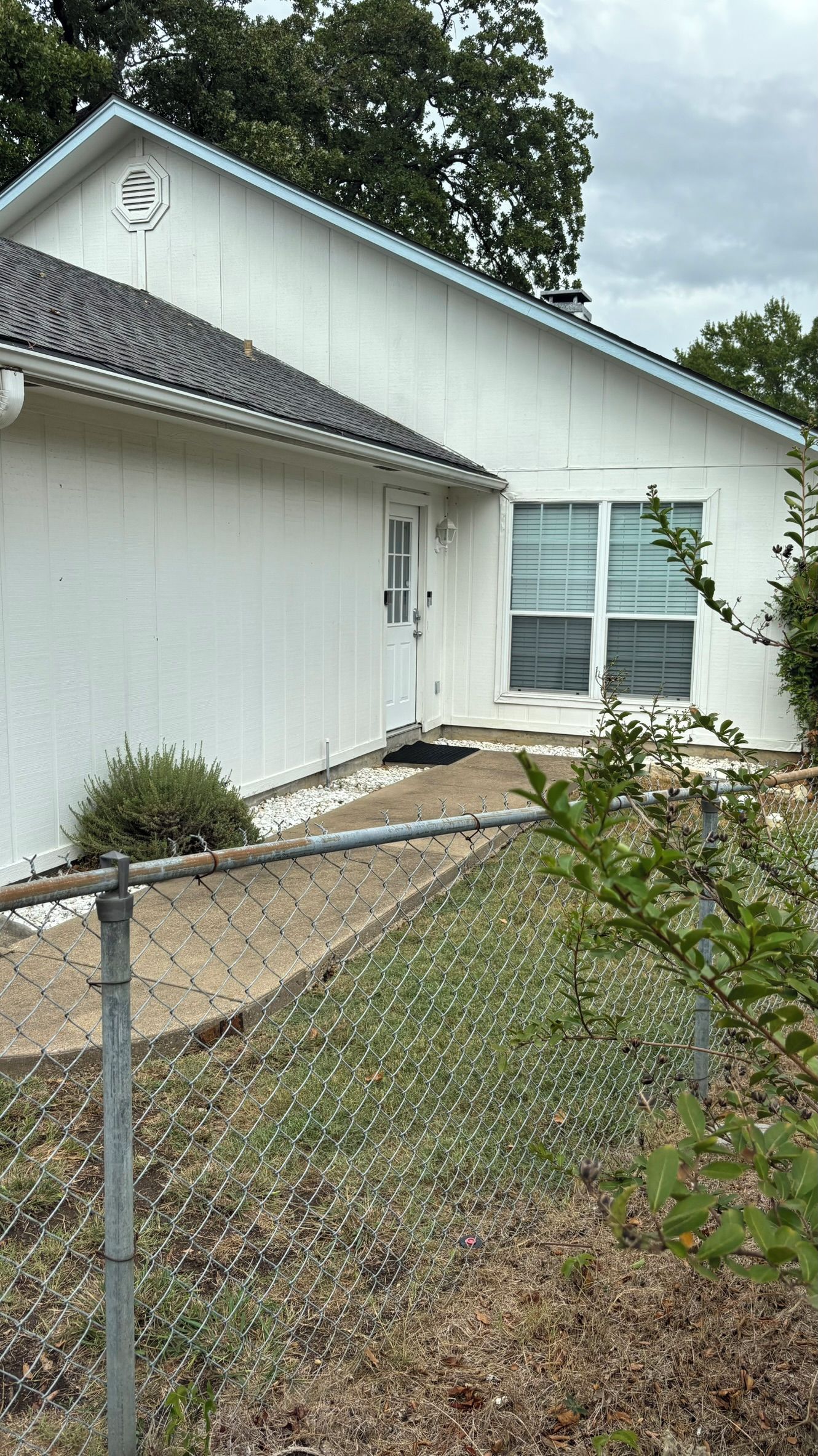 A single-story building with a white exterior, a front door, and a window with shutters.