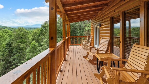 Una terraza de madera con sillas y una mesa, con vistas a un paisaje boscoso.