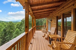 A wooden deck with chairs and a table, overlooking a forested landscape.
