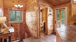 Interior de una cabaña de madera con una zona de cocina, una mesa de comedor y un baño visible a través de una puerta abierta.