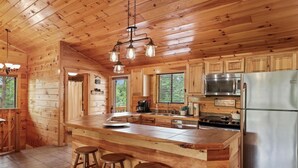 Cocina de cabaña de madera con una isla grande, electrodomésticos de acero inoxidable y una lámpara colgante.