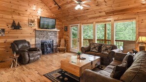 Interior acogedor de una cabaña con chimenea, mobiliario de cuero y ventanas amplias con vista al bosque.