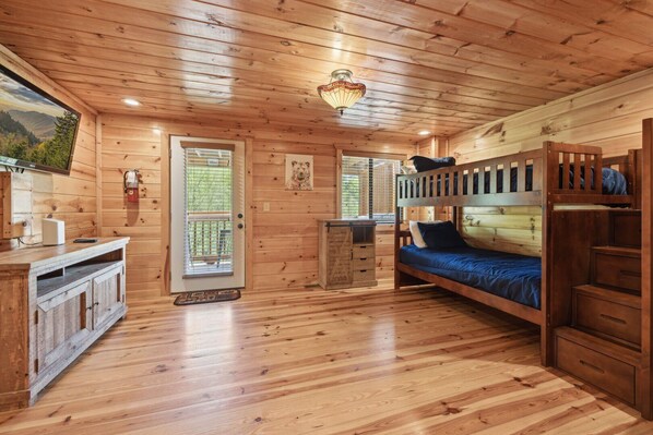 A wooden cabin interior with a bunk bed, a desk, and a small kitchenette.