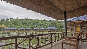 A wooden deck with a railing overlooking a body of water and a row of blue-roofed buildings. - Blue Resort and Spa Koh Chang (Ko Chang)