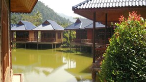 A traditional wooden house with a tiled roof, situated over a body of water, surrounded by lush greenery. - Blue Resort and Spa Koh Chang (Ko Chang)