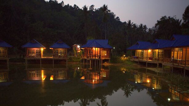 A series of wooden chalets with blue roofs, reflecting in a calm body of water, surrounded by dense forest. - Blue Resort and Spa Koh Chang (Ko Chang)