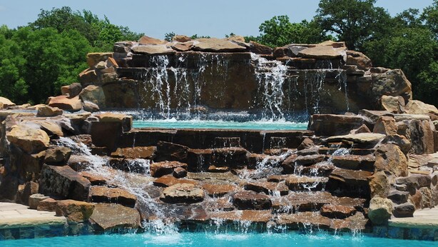 Une piscine naturelle formée par une cascade rocheuse, avec de l’eau claire et une structure en pierre.