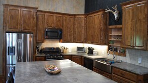 Une cuisine avec des meubles en bois, des appareils électroménagers en acier inoxydable, un four à micro-ondes, un grille-pain et un crâne de cerf servant de décoration.