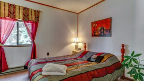 A bedroom with a large bed, a nightstand with a lamp, a window with curtains, and a painting on the wall. - Beautiful Red Chalet with  Hot-Tub and Sauna in Poconos (Long Pond)