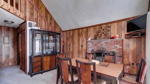 Un coin repas avec une table et des chaises en bois, un buffet contenant de la verrerie et une cheminée en briques.