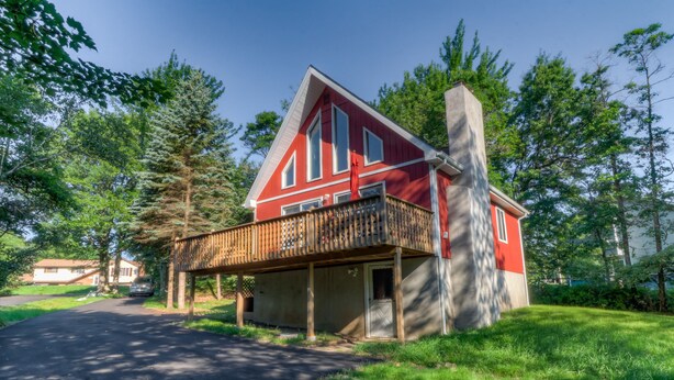 A red house with a balcony, surrounded by trees and a clear sky. - Beautiful Red Chalet with  Hot-Tub and Sauna in Poconos (Long Pond)